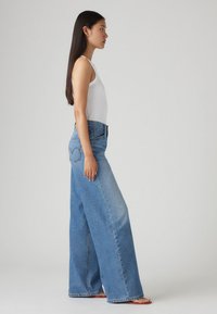 Vaqueros de pierna ancha de color azul claro, hechos de denim, con una cintura alta, diseño de cinco bolsillos y un distintivo bordado en los bolsillos traseros.