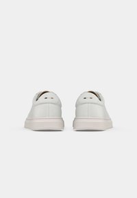 Weiße Leder-Sneaker mit glatter Textur, die ein niedriges Profil, eine runde Zehenpartie und minimalistische Akzente in Schwarz und Gold an der Ferse aufweisen.