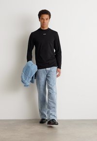 Musthave musta pika varrukaga särk, laiad heledad sinised teksad ja mustad kingad. Denim-jakk on vasaku käe peal. Üksildane taust.