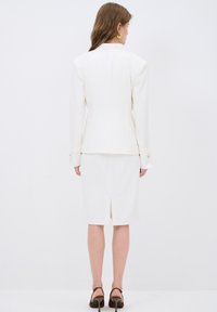 White blazer and pencil skirt set, featuring a tailored fit, smooth texture, rear slit, and gold-button accents on the sleeves.