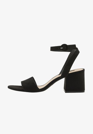Sandale noire en daim à bout ouvert, talon bloc, bride de cheville et fermeture à boucle ronde.