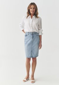 Lichtblauwe denim pencil skirt met een rits aan de voorkant, twee zakken en een hoge taille. Gecombineerd met een witte blouse en witte sandalen.