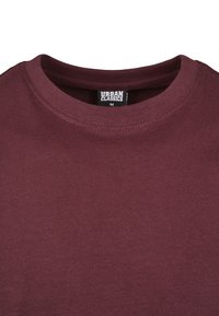 Burgundi színű póló, kerek nyakú, puha anyagból készült. A belsejében található "URBAN CLASSICS" címke, M-es méret. Sima textúra és egységes szín.