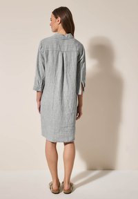 Abito a righe grigie e bianche con vestibilità rilassata, maniche a tre quarti e dettaglio della piega sul retro. Tessuto morbido e lunghezza fino a metà coscia.