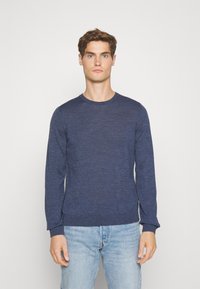 Pulover lung cu maneci lungi, de culoare albastru marin, realizat dintr-un material texturat, cu mansete și tiv cu bandă, purtat cu blugi de culoare albastru deschis.