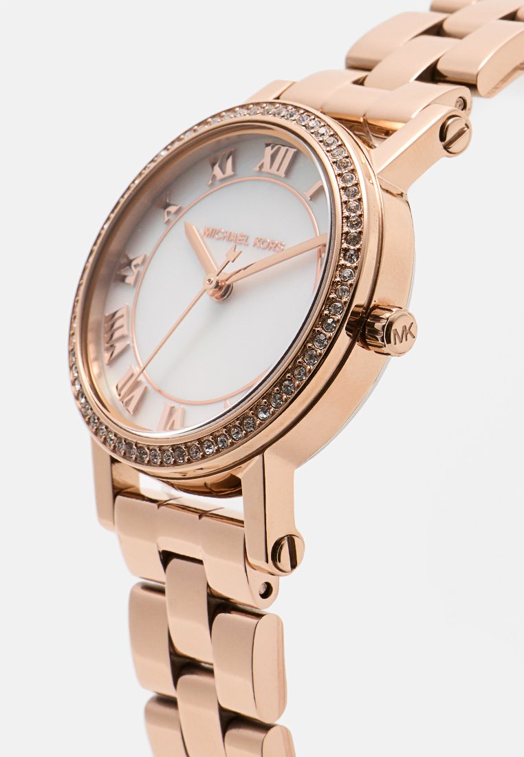 Montre en métal doré rose avec un cadran blanc, des chiffres romains et une lunette ornée de cristaux. Le bracelet présente un design à maillons.