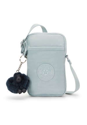 Bolso bandolera de tela azul claro con logo circular en relieve, cierre de cremallera y un llavero de mono esponjoso azul oscuro.