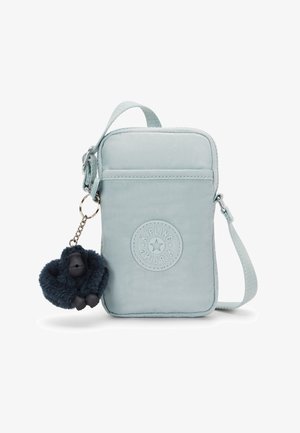 Sac bandoulière en tissu bleu clair avec logo circulaire embossé, fermeture éclair, et un porte-clés en forme de singe duveteux bleu foncé attaché.