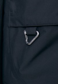 Black fabric with a smooth texture featuring a pocket and a metallic carabiner clip attached, set against a plain background.
