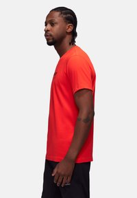 Rød bomulds T-shirt med rund hals, korte ærmer og et trykt logo på forsiden. Stoffet har en glat tekstur.
