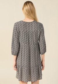 Vestido de flores negro y crema con mangas de tres cuartos, cintura fruncida y dobladillo con volantes. Tela ligera, diseño hasta la rodilla.