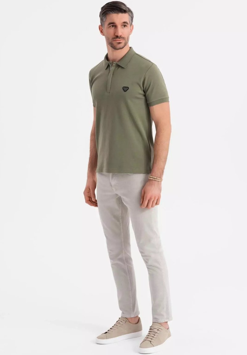 Oliivivihreä polo-paita lyhyillä hihoilla ja klassisella kauluksella, yhdistettynä vaaleanharmaisiin slim-fit-housuihin ja beigeihin tennareihin.