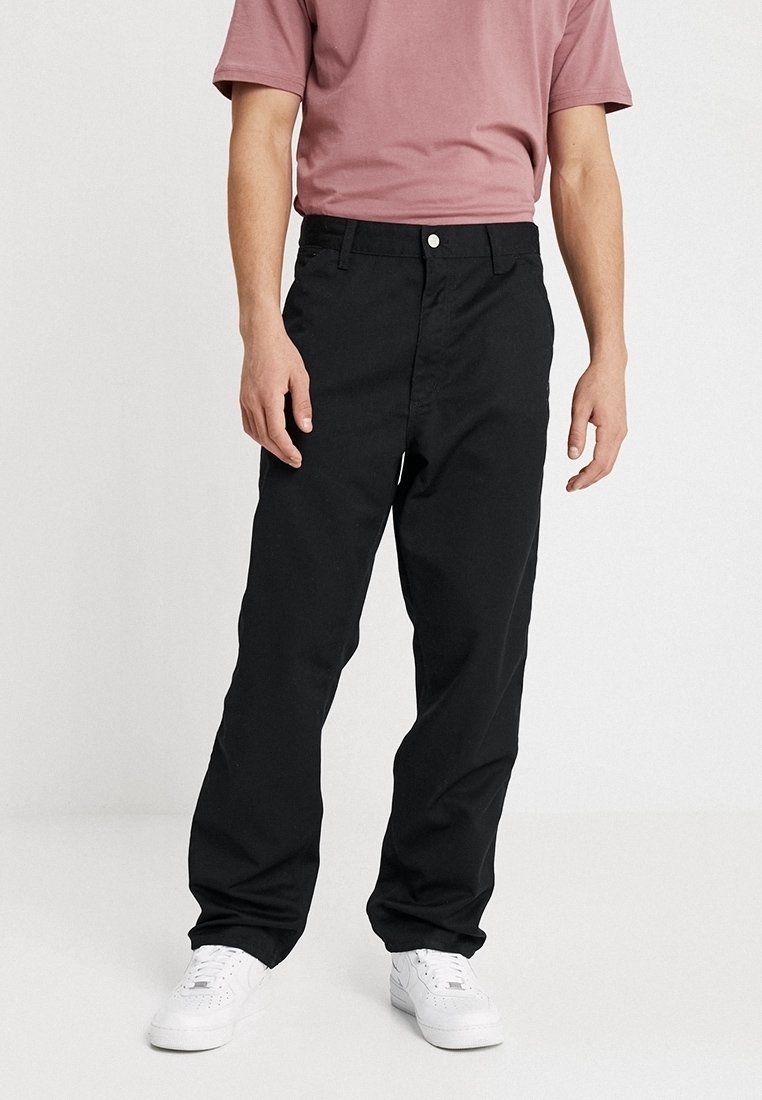 Czarne spodnie o prostym kroju, z klasycznym zapięciem na guzik i zamek błyskawiczny, wykonane z wytrzymałej bawełnianej tkaniny. Noszone z różową koszulą.