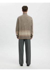 Bēša vilnas džemperis ar augstu apkakli, pie apakšmalas horizontāls gradienta raksts maigos toņos. Kombinēts ar pelēkām biksēm.