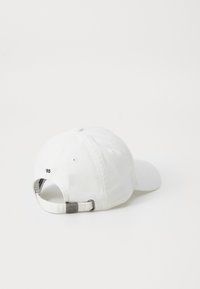Casquette de baseball blanche en coton avec une visière incurvée, système de réglage avec boucle en métal, et détail brodé "85" à l'arrière.