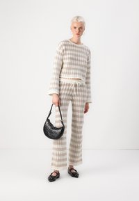 Virkad topp och byxor i beige och gräddvita ränder, med dragsko i midjan. Svart handväska med nitar. Svarta platta skor.