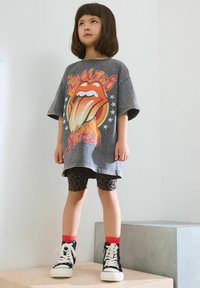 Sivi oversize majica s grafikom Rolling Stones, tajice s leopardskim uzorkom, crvene čarape do gležnjeva i crne visoke tenisice.