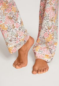 Blumen-Pyjama-Hosen in Pastellfarben aus leichtem Stoff, mit einer Vielzahl von kleinen Blumen und umgeschlagenen Säumen, kombiniert mit baren Füßen.