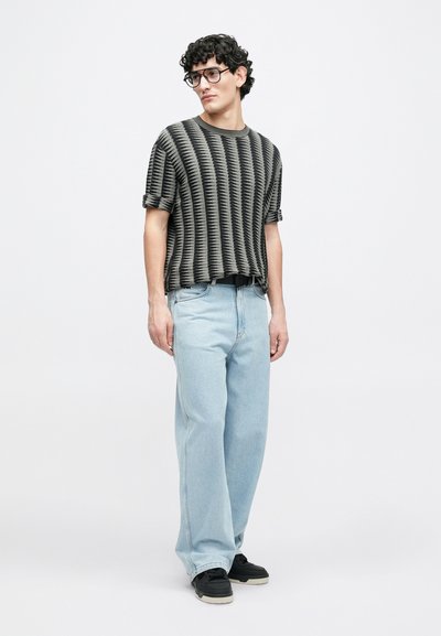 T-shirt en maille rayée noire et grise avec manches retroussées, associée à un jean bleu clair ample et des baskets noires. Design simple et décontracté.