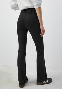 Leggings noirs avec une coupe évasée, tissu doux, taille élastique et détails minimaux. Assortis à des chaussures de sport foncées.