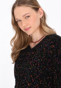 Czarny puszysty sweter z wielokolorowymi drobinkami, z szerokim dekoltem. Noszony z czerwoną naszyjnikiem choker oraz małymi srebrnymi kolczykami w kształcie kółek.