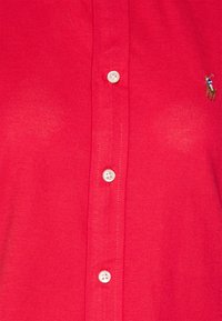 Polo shirt rosso con bottoni bianchi lungo il centro e un piccolo logo ricamato di un giocatore di polo sul lato destro.