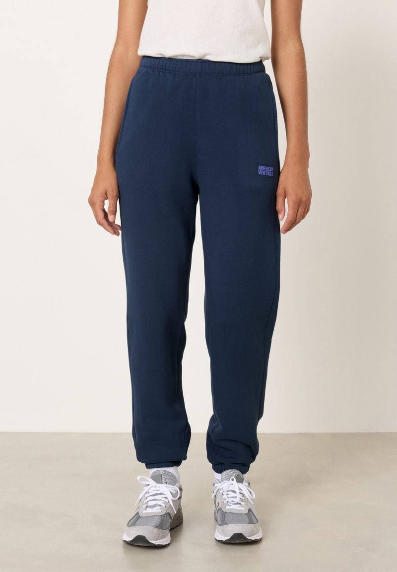 Tmavomodré bavlnené tepláky s voľným strihom, elastickým pásom a bočnými vreckami. Na stehne je tmavomodré logo "American Vintage".