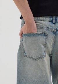 Los jeans de denim azul claro cuentan con un bolsillo trasero estándar con costuras visibles. La tela tiene una textura ligeramente desgastada, lo que resalta un aspecto casual.