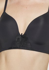 Black bra with smooth cups and a deep V neckline. Features lace detailing with a bow at the center. Adjustable thin straps.