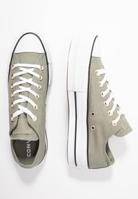 Green canvas sneakers with white rubber soles, black trim, and gold eyelets. Featuring white laces and a textured toe cap.