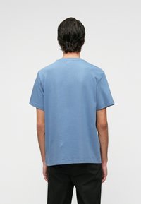 Világoskék pamut póló rövid ujjakkal, kerek nyakkivágással és egyenes szegéllyel. Simább textúra, minimális márkázás és laza fit.