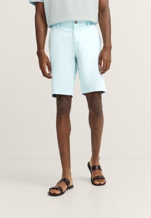 Hellblaue Shorts mit entspannter Passform, Stoffstruktur und Knopfverschluss, kombiniert mit schwarzen flachen Sandalen. Einfaches, lässiges Design.