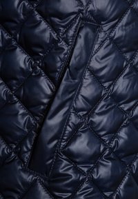 Pikowany granatowy materiał puchowy o błyszczącej powierzchni, z diamentowymi wzorami i ukrytym detalem zapięcia.