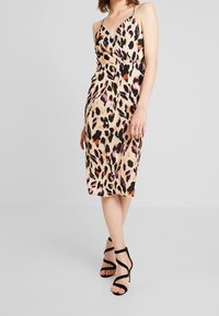 Leopard print dress in smooth fabric, featuring a V-neck, spaghetti straps, and cinched waist, complemented by a fitted silhouette and knee-length cut.