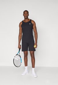 Svart idrettstopp med logo, svarte shorts, hvite sneakers, holder en tenniskølle og en gul tennisball. Enkel, funksjonell design.
