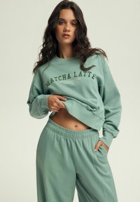 Miętowy zestaw bluz i spodni dresowych z nadrukowanym tekstem na górze, charakteryzujący się luźnym krojem i miękką teksturą.