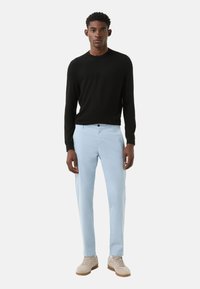 Zwarte trui met lange mouwen, lichtblauwe broek en beige sneakers. Eenvoudig ontwerp, zachte textuur en casual stijl met een getailleerde pasvorm.