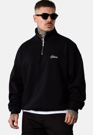 Black zip-up pullover with a high collar, featuring embroidered logo on the chest, oversized fit, and ribbed cuffs. Soft fleece texture.