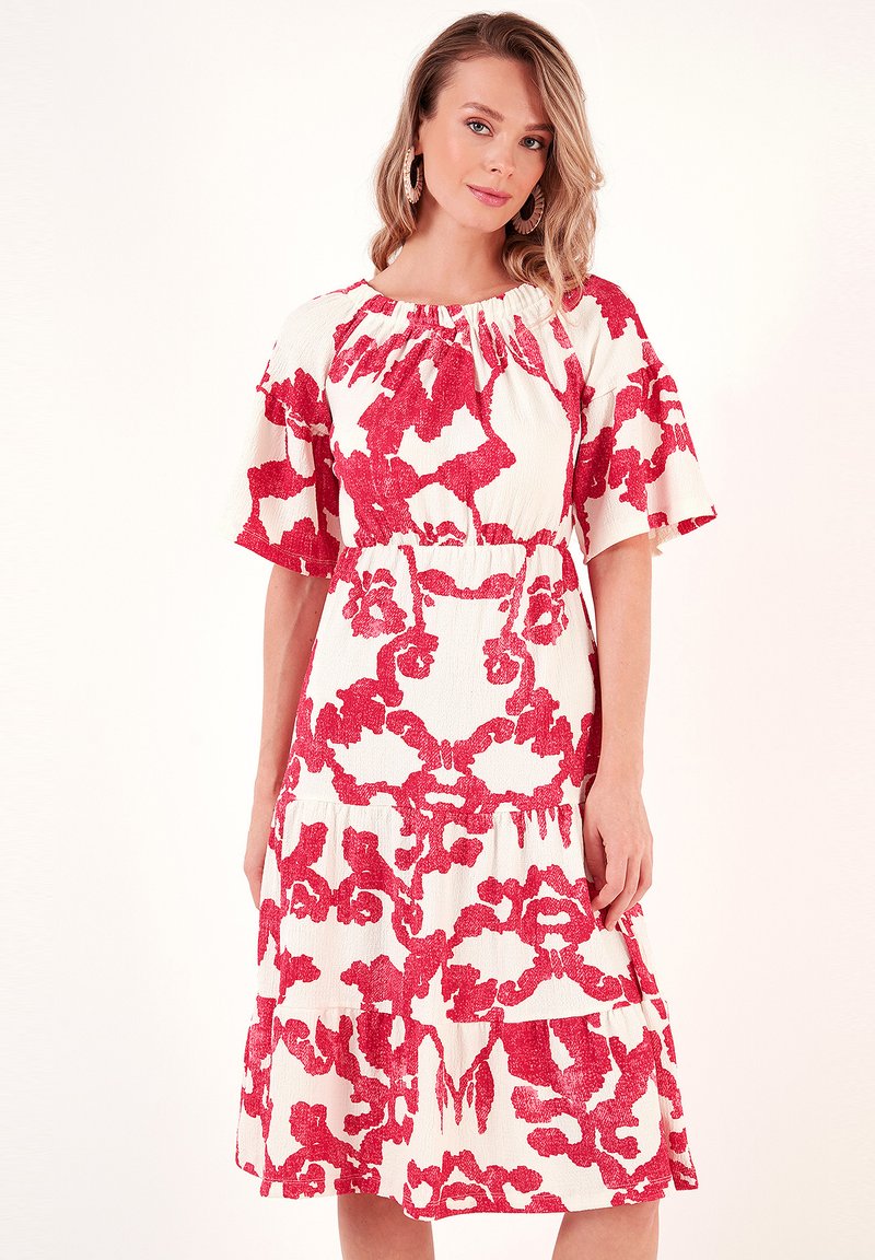 White dress with bold red floral pattern, short flutter sleeves, gathered neckline, and a tiered hem. Made from a textured fabric.
