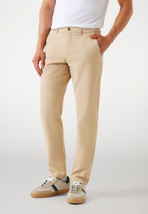 Beige Hosen aus Baumwollmischung, mit geradem Schnitt, Fronttaschen und einem einzelnen Metallknopfverschluss. Tragen mit grauen und grünen Turnschuhen.