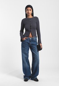 Szary, prążkowany, długi rękaw z guzikami z przodu, w połączeniu z luźnymi, niebieskimi dżinsami. Czarna torebka i płaskie buty dopełniają strój.