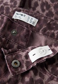 Lilla mustriga kangas, millel on reguleeritav nupp sees vöökoha juures ja riideetikett, mis näitab suurust ja päritolu.