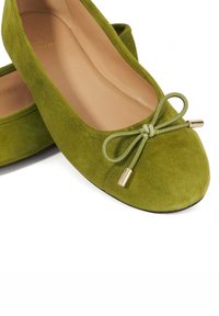 Green suede ballet flats with a rounded toe and a matching bow. The bow features a metal tip accent. Smooth inner lining. Black sole.