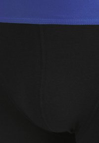 Zwarte sportleggings met een gladde textuur, met een nauwsluitende pasvorm en een contrasterende paarse elastische band in de taille.