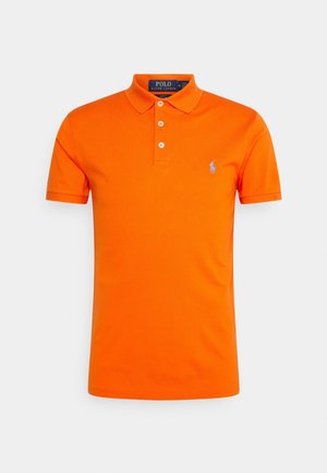 Jasnopomarańczowa koszulka polo z krótkim rękawem, z trzema białymi guzikami i małym niebieskim haftowanym logo na lewej piersi.