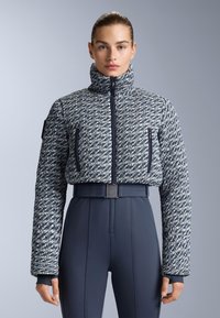 Jakna s uzorkom u mornarskoj plavoj i bijeloj boji, s visokim ovratnikom, zatvorenim džepovima i rebrastim manžetama, nosi se preko prilagođenih mornarskih hlača s remenom.