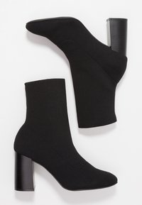 Botas negras hasta el tobillo con parte superior de punto, puntera redondeada y un tacón cuadrado de 10 cm con textura estriada. Sin cierres visibles ni adornos.