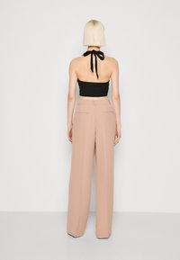 Svart halterneck crop-top med bindesnor i ryggen, sammen med høyt midjebånd, vide bukser i lys rosa med to baklommer.