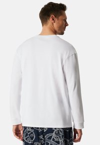 Camisa blanca de manga larga hecha de tela suave, con un cuello redondo y puños, combinada con pantalones cortos oscuros de estampado.