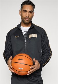 Čierna mikina na zips Nike s nápisom "BOSTON" v zlatom písmene, elegantný dizajn, spárovaná s oranžovým basketbalom s čiernym logom.